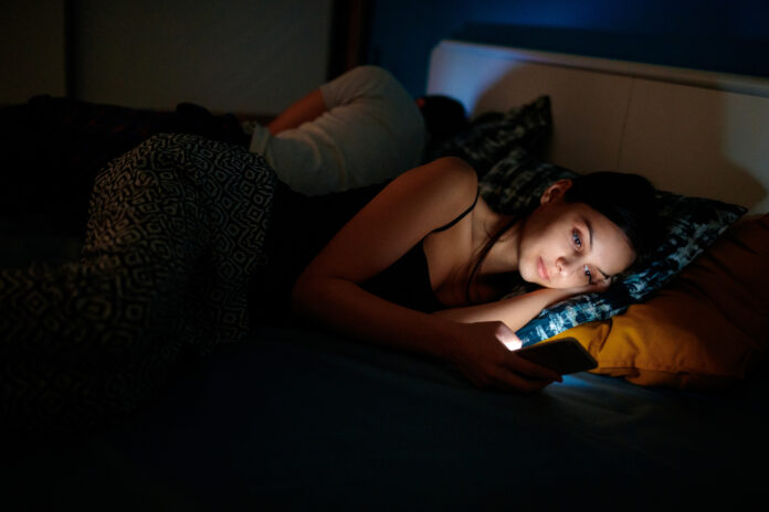 She is checking her smartphone at bedtime