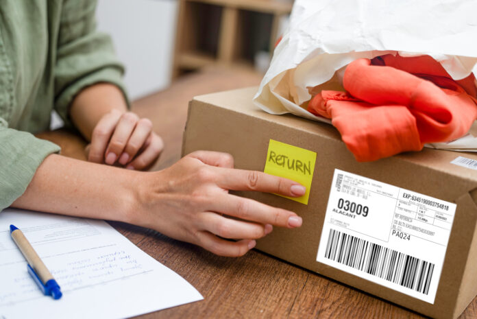 Woman pastes inscription Return on yellow sticker on cardboard box on wooden desk in premise